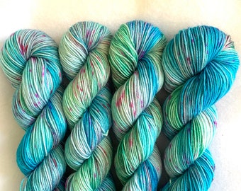 May include: Three skeins of yarn in shades of teal, green, and pink. The yarn is hand-dyed and has a speckled appearance.