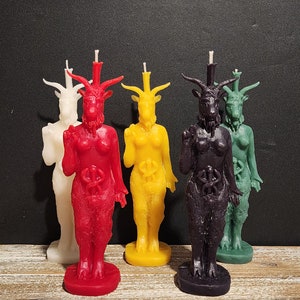 Può includere: Cinque candele di Baphomet in vari colori: bianco, rosso, giallo, viola e verde. Ogni candela raffigura una figura con testa di capra, corna, barba e una torcia. Le candele sono su una superficie di legno.