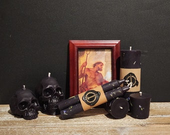 May include: Black skull-shaped candles and black pillar candles with dried flowers and a framed image of a man holding a trident. The candles have labels with a circle and a sword.