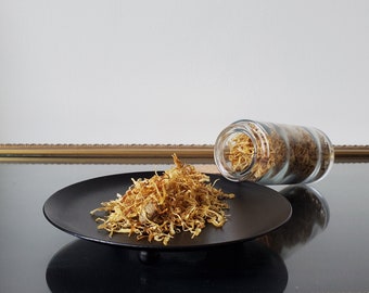 May include: A black plate with a pile of dried, golden yellow flower petals. A clear glass jar filled with the same petals is tipped over on the plate.