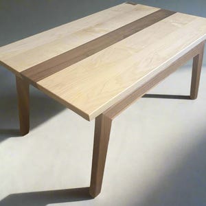 May include: A wooden table with a light wood top and a dark wood stripe down the center. The table has four legs.