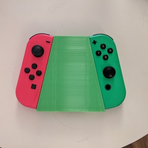 May include: A green and pink Nintendo Switch console with a green 3D printed case. The console is in handheld mode with the controllers attached.