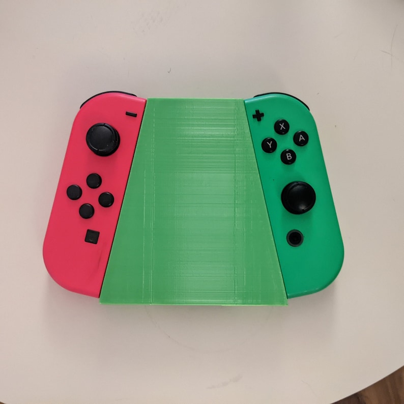 May include: A green and pink Nintendo Switch console with a green 3D printed case. The console is in handheld mode with the controllers attached.