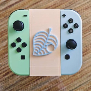 May include: A light green and light blue Nintendo Switch console with a custom faceplate featuring a light blue leaf design. The console has a black button layout.