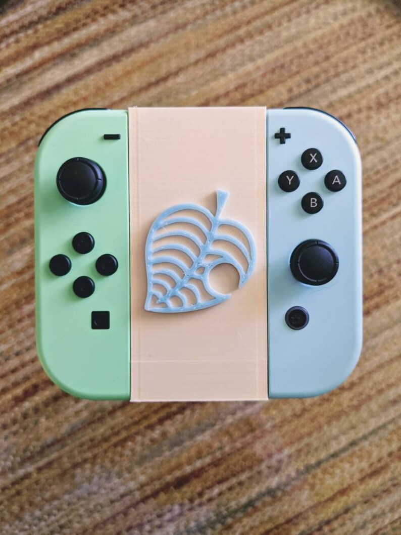 May include: A light green and light blue Nintendo Switch console with a custom faceplate featuring a light blue leaf design. The console has a black button layout.