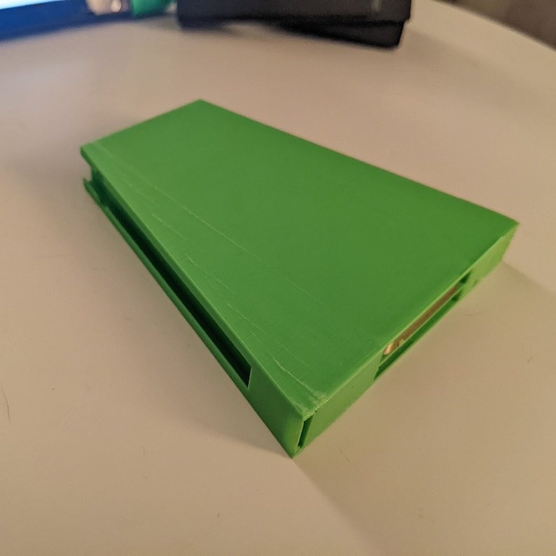 May include: A bright green 3D printed case with a slot for a small device. The case has a smooth, slightly textured surface.