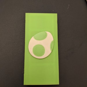 May include: A green and white egg-shaped object with green spots. The object is made of a smooth, textured material.