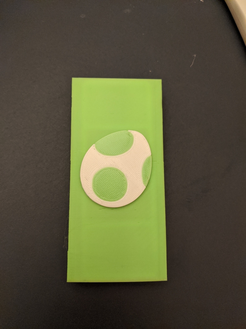 May include: A green and white egg-shaped object with green spots. The object is made of a smooth, textured material.