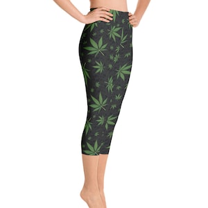 May include: Cropped leggings with a dark gray background and a repeating pattern of green cannabis leaves. The leggings are high-waisted and reach to the mid-calf. The fabric appears to be a soft, stretchy material.