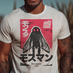Puede incluir: Camiseta blanca con un gráfico de una polilla negra con ojos rojos y un fondo rojo. Texto japonés está arriba y abajo del gráfico de la polilla. También se incluye el texto "West Virginia". La camiseta la lleva una persona.