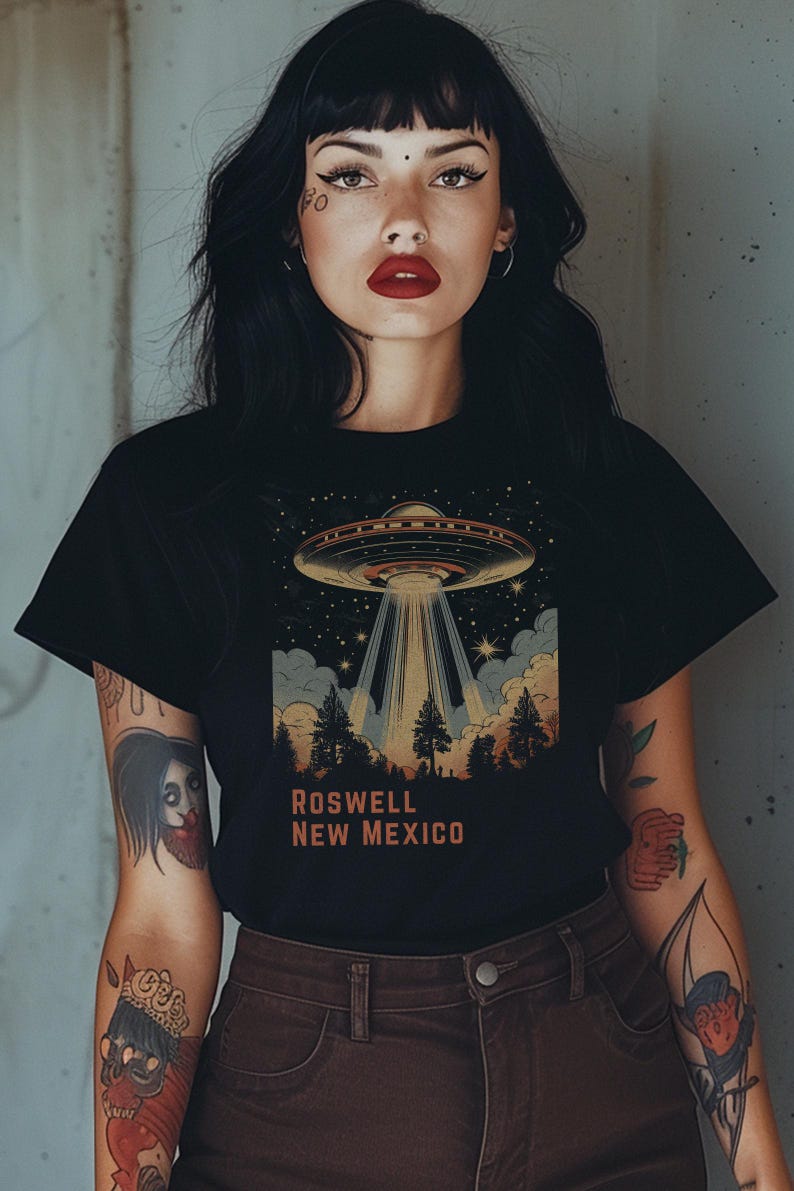 Puede incluir: Camiseta negra con una ilustraci&oacute;n retro de un OVNI que proyecta luz sobre un bosque, con el texto "ROSWELL NEW MEXICO" en naranja. La camiseta tiene cuello redondo.