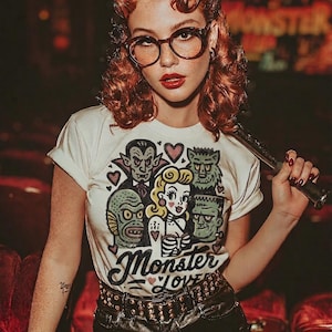 Pu&ograve; includere: T-shirt color crema con grafica di mostri classici e la scritta "Monster Love". Il design include Dracula, il mostro di Frankenstein e una donna. La maglietta &egrave; abbinata a pantaloncini di pelle neri e una cintura borchiata.
