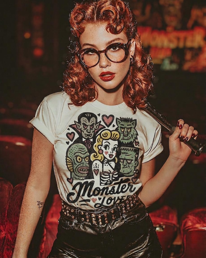 Pu&ograve; includere: T-shirt color crema con grafica di mostri classici e la scritta "Monster Love". Il design include Dracula, il mostro di Frankenstein e una donna. La maglietta &egrave; abbinata a pantaloncini di pelle neri e una cintura borchiata.