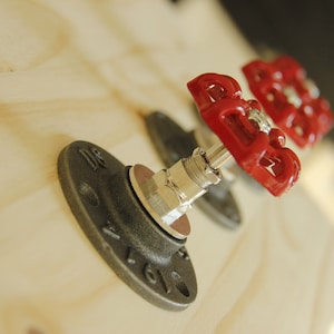 Peut inclure: Deux poignées de vanne industrielles en métal noir avec des brides en métal noir montées sur une surface en bois clair.