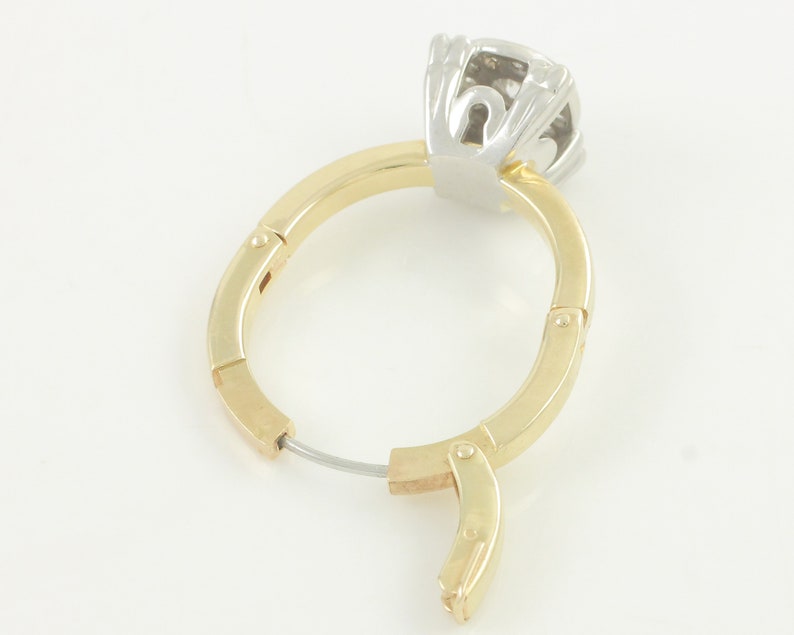 May include: A pair of gold hoop earrings with a hinged closure. The earrings are made of two-toned metal, with a gold band and a silver top. The top of the earring features a diamond-shaped stone.