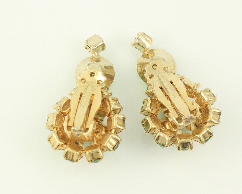 Peut inclure: Une paire de boucles d'oreilles clips en or avec un groupe de strass vert clair.