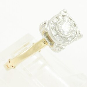 May include: A gold and white diamond engagement ring with a round center stone and a halo of smaller diamonds.