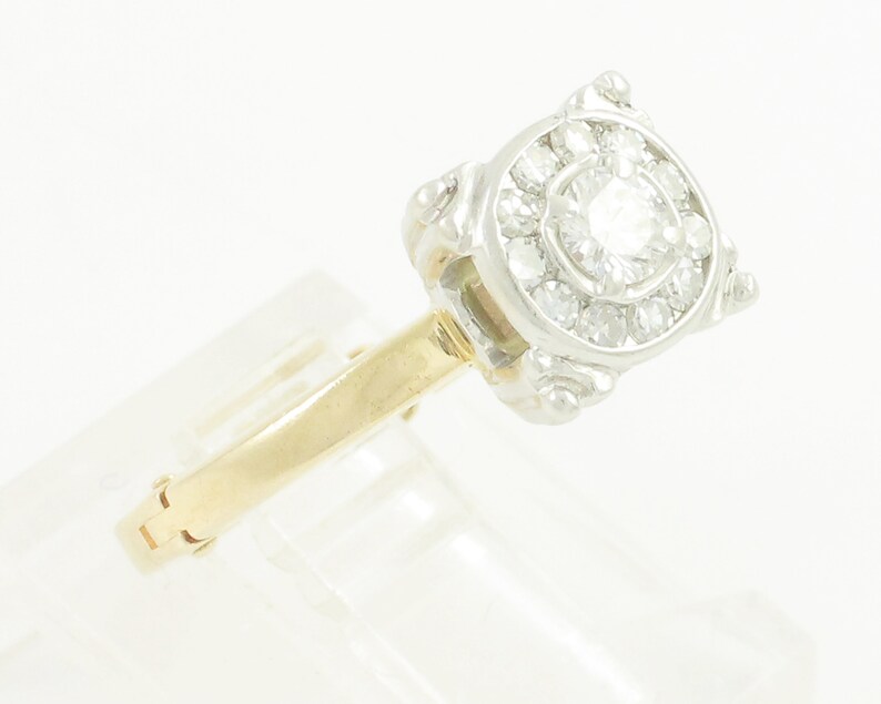 May include: A gold and white diamond engagement ring with a round center stone and a halo of smaller diamonds.