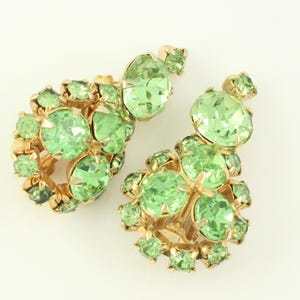 Peut inclure: Une paire de boucles d'oreilles en strass vert avec des montures dor&eacute;es. Les boucles d'oreilles sont compos&eacute;es de plusieurs strass ronds regroup&eacute;s.