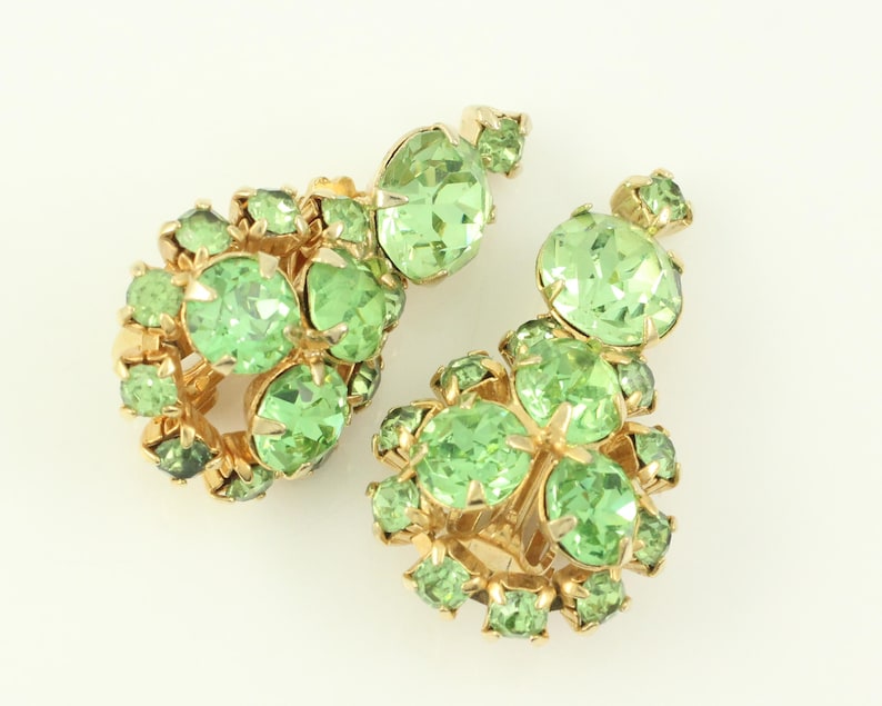 Peut inclure: Une paire de boucles d'oreilles en strass vert avec des montures dor&eacute;es. Les boucles d'oreilles sont compos&eacute;es de plusieurs strass ronds regroup&eacute;s.