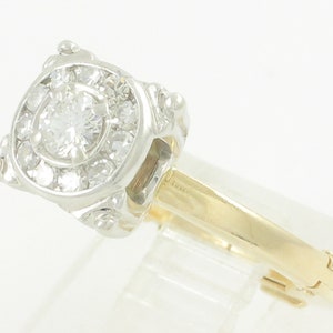 May include: A gold and white diamond engagement ring with a round center stone surrounded by smaller diamonds. The ring has a delicate, ornate design.