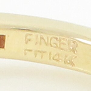 May include: Close-up of a gold ring with the inscription "Finger Fit 14K" on the inside band.