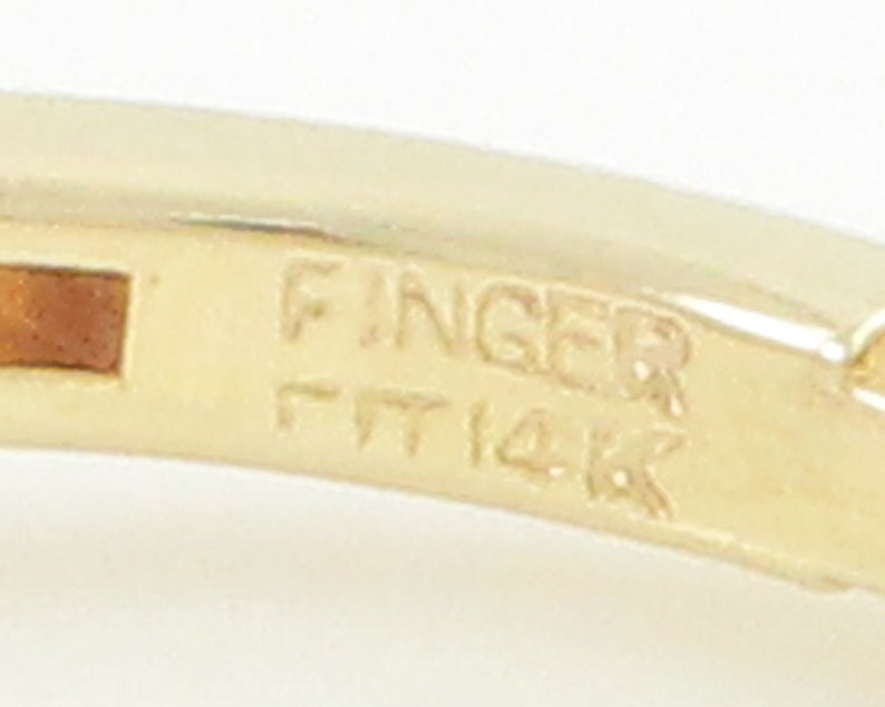 May include: Close-up of a gold ring with the inscription "Finger Fit 14K" on the inside band.