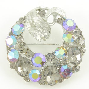 May include: A silver tone brooch with a swirl design and iridescent rhinestones. The brooch is in the shape of a crescent moon.