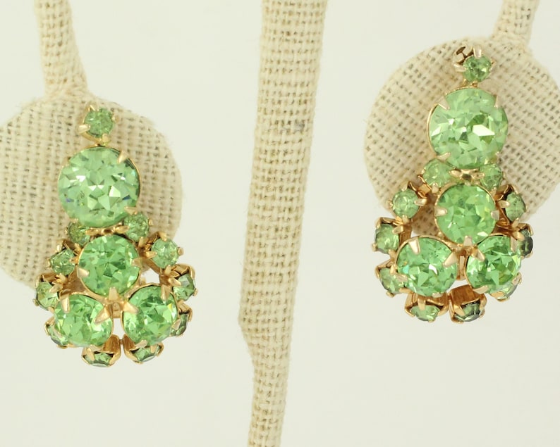 Peut inclure: Une paire de boucles d'oreilles pendantes avec un groupe de strass vert clair sertis dans un m&eacute;tal dor&eacute;.