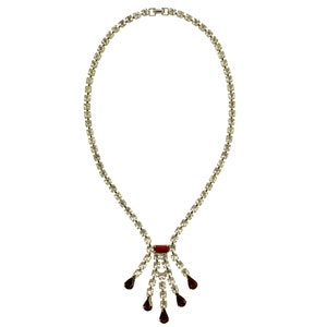 May include: A silver necklace with a teardrop-shaped red stone pendant and a row of clear stones.