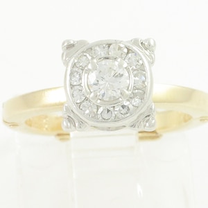 May include: A gold and white diamond engagement ring with a round center stone and a halo of smaller diamonds.