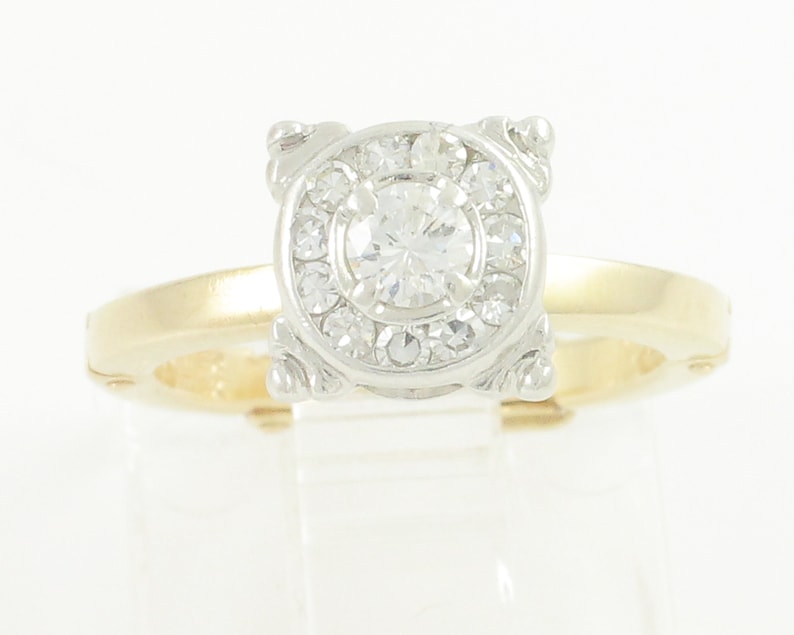 May include: A gold and white diamond engagement ring with a round center stone and a halo of smaller diamonds.