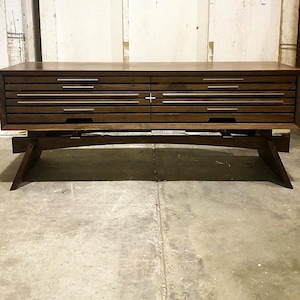May include: A dark brown wooden coffee table with a unique design. The table has two drawers with silver handles and a curved base.