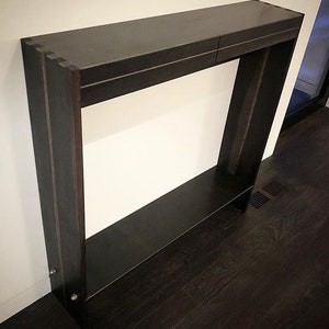 May include: A dark wood console table with two shelves. The table has a simple, modern design and is perfect for a hallway or entryway.