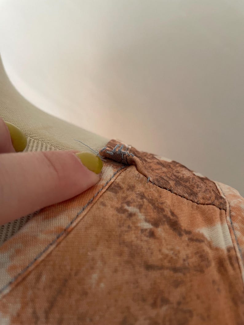 May include: Close-up of the neckline of a brown and white tie-dye shirt. The shirt has a seam along the neckline and the fabric is soft and textured.