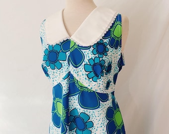 May include: A white sleeveless dress with a large blue and green floral print. The dress has a white Peter Pan collar with a lace trim.