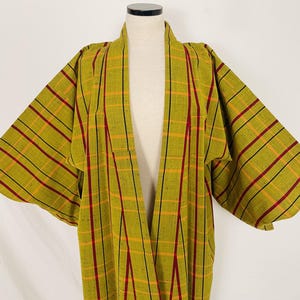 May include: Olive green kimono-style robe with a plaid pattern. The plaid features red, yellow, and black stripes. The robe is displayed on a mannequin against a white background. The robe has wide sleeves and an open front.