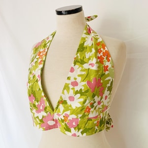 May include: A floral halter top with a vibrant pattern of green, white, pink, and orange flowers. The top is displayed on a mannequin, showcasing its design and shape. The fabric appears to be lightweight.