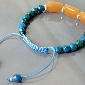 Puede incluir: Un brazalete de piedras azules y naranjas con cierre de cordón azul anudado. El brazalete presenta cuentas de piedras azules facetadas y tres cuentas rectangulares de piedras naranjas.