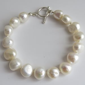 May include: A white pearl bracelet with a silver toggle clasp. The pearls are large and round, and the bracelet is approximately 18 cm in length.