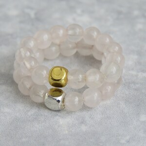 Puede incluir: Un brazalete de doble cadena hecho con cuentas de cuarzo rosa claro con cuentas espaciadoras doradas y plateadas.