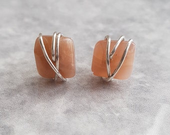 May include: A pair of earrings featuring peach-colored stones wrapped in silver wire.