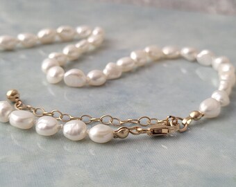 May include: A delicate pearl necklace with a gold chain clasp. The pearls are white and have an irregular shape.