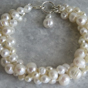 May include: A white pearl bracelet with a silver clasp. The pearls are of varying sizes and are arranged in a twisted pattern.
