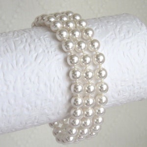 May include: A white pearl bracelet with three rows of pearls. The bracelet is made of faux pearls and is a classic and elegant accessory.