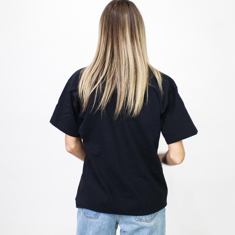 May include: A black short-sleeved t-shirt and blue jeans. The person is facing away from the camera. The t-shirt is a solid black color. The jeans are light blue.