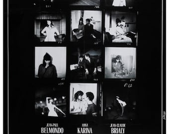 May include: A black and white movie poster for the film "Une Femme Est Une Femme" (A Woman is a Woman) directed by Jean-Luc Godard. The poster features a series of black and white photographs of the film's stars, Jean-Paul Belmondo, Anna Karina, and Jean-Claude Brialy.