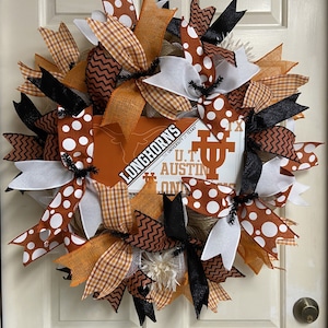 May include: A decorative wreath featuring a University of Texas Longhorns theme. The wreath is adorned with orange, white, black, and brown ribbons in various patterns, including polka dots, gingham, and chevron. The center displays the Longhorns logo and text.