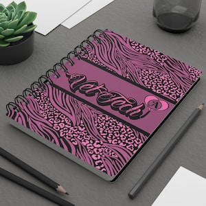 Puede incluir: Un cuaderno de espiral con un diseño de estampado animal rosa y negro. El cuaderno presenta el texto "Vet Tech" en una fuente cursiva, con un corazón y la letra "A" en el lado derecho. La portada tiene un estampado de cebra y leopardo.