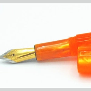 May include: A bright orange fountain pen with a gold-coloured nib and cap. The pen is made of a marbled acrylic material.